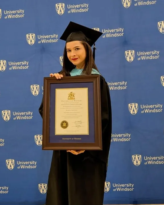 Mar de la Hoz in cap and gown, holding her Master of Education diploma at the University of Windsor.